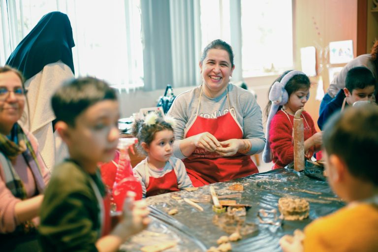 Smiling teacher leading an engaging art class with children crafting at a table indoors.