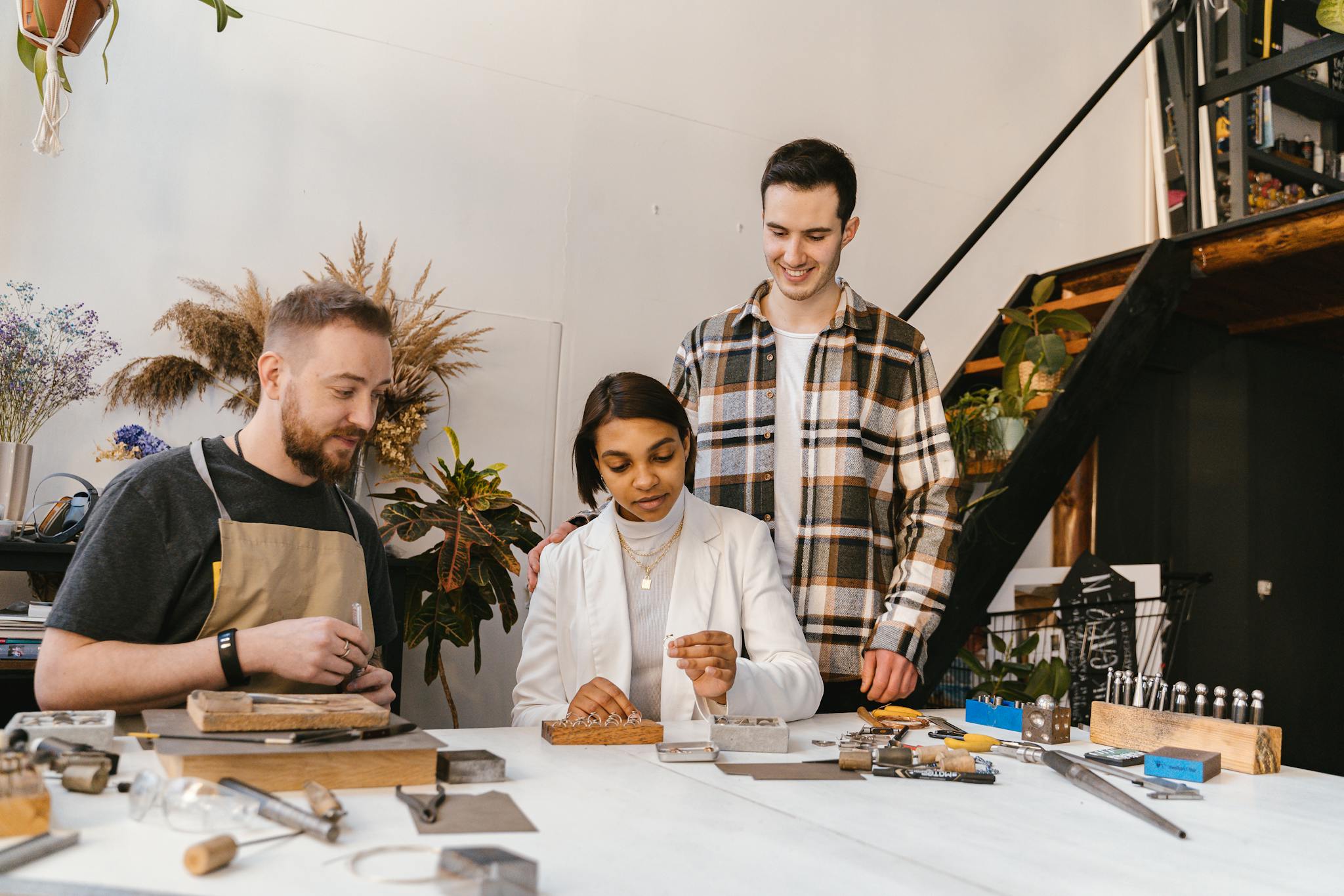 Three adults engaged in a jewelry making workshop, surrounded by tools and materials.